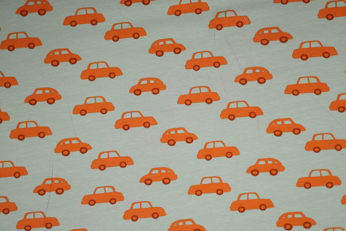 Kinderstoff aus Baumwolle mit orangen Autos auf hellgrauem Hintergrund.